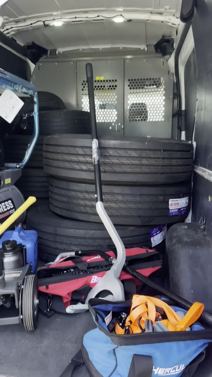 Stacked commercial truck tires, a tire iron, and a floor jack loaded inside the service van